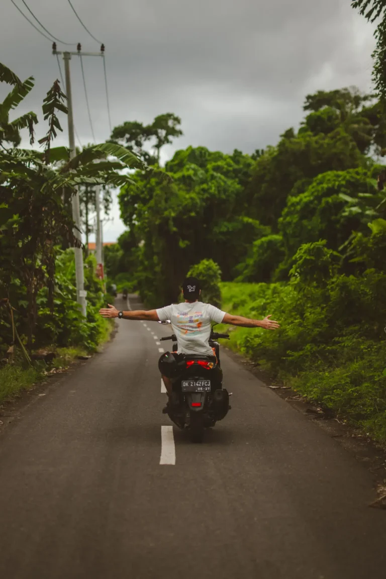 A rider seen from behind with arms outstretched on an empty road lined with jungle in Bali