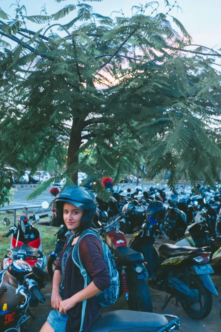 A woman in a helmet with a backpack beside a crowded scooter parking area in Bali