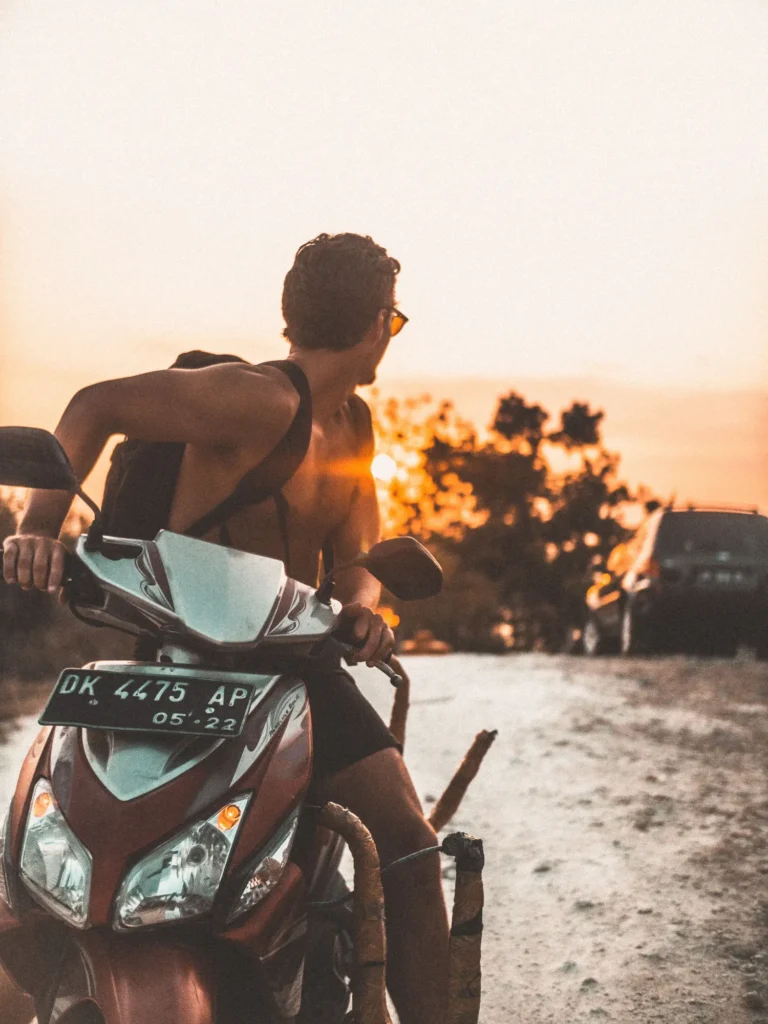 A rider sitting on a scooter on a sandy track at sunset in Bali