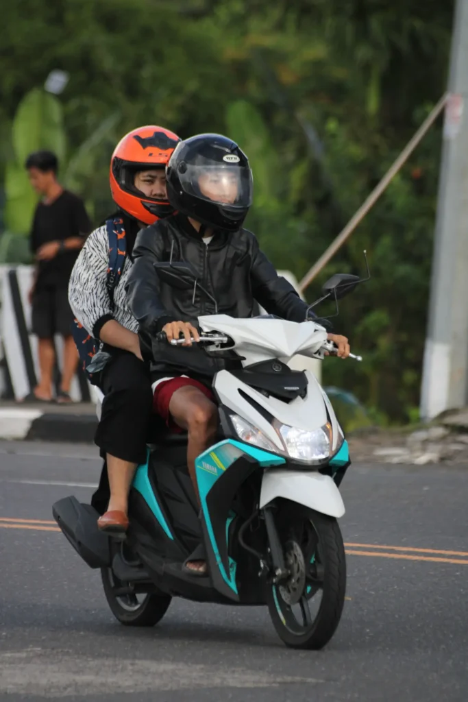Two helmeted riders sharing one scooter in traffic in Bali